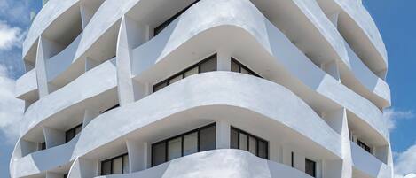 A multi-story hotel with a unique wavy architectural design, multiple balconies, and a visible entrance with a ramp.