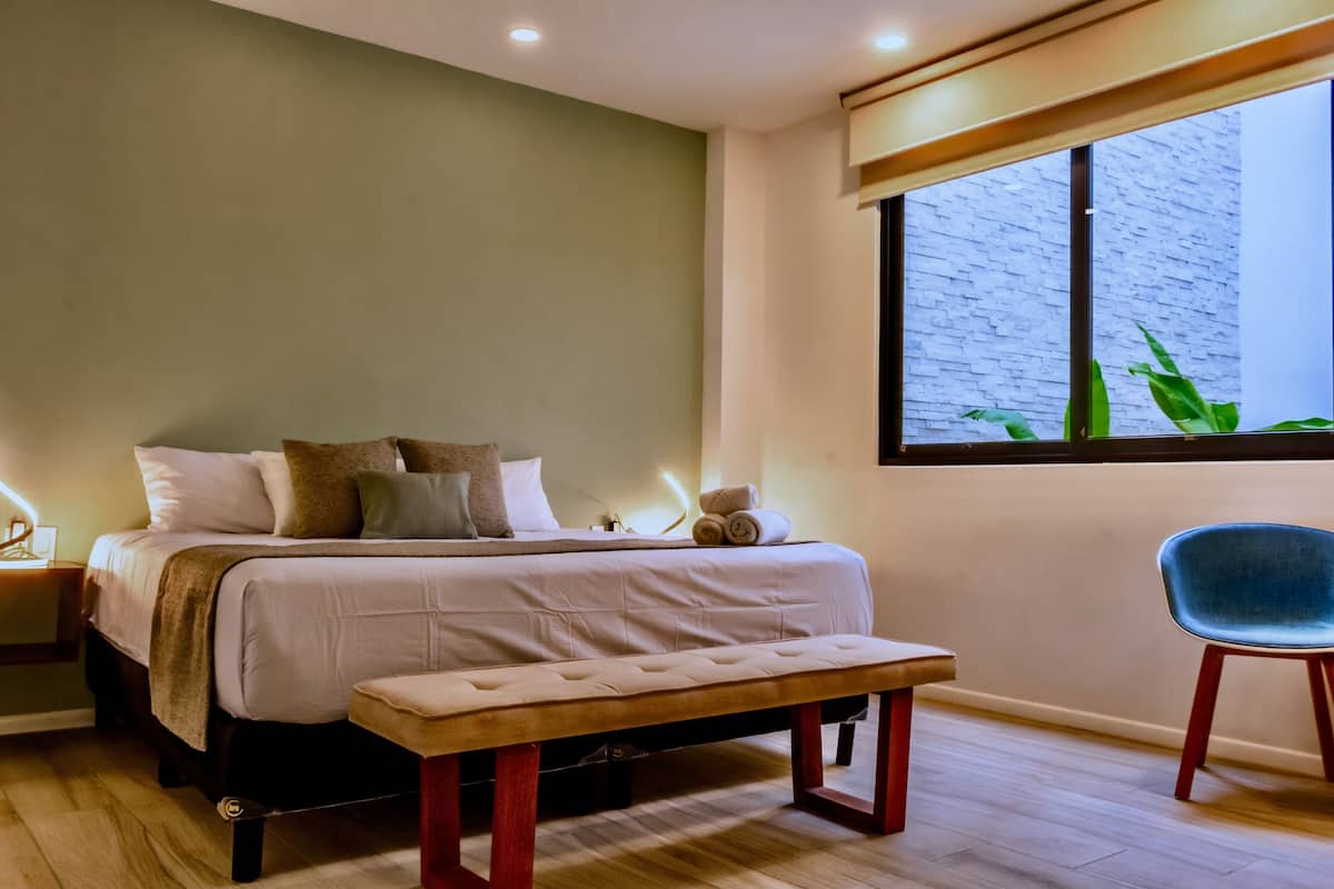 Une chambre à coucher comprenant un lit, un banc, une chaise, une table de chevet et une fenêtre donnant sur un beau paysage.