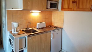 Une cuisine compacte avec des meubles en bois, un four à micro-ondes encastré, un grille-pain, un évier et un petit réfrigérateur.