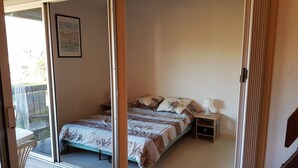 Une chambre à coucher comprenant un lit, une table de chevet et une porte-fenêtre coulissante donnant sur un balcon.