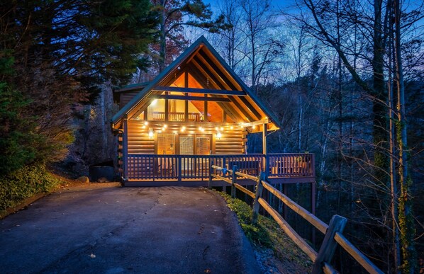 A log cabin with a wooden deck, surrounded by trees. - Seasonal Outdoor Pool 🐻 Family Friendly🍂Cozy Cabin 🏔3 mi to Strip 🍁Hot Tub (Gatlinburg)