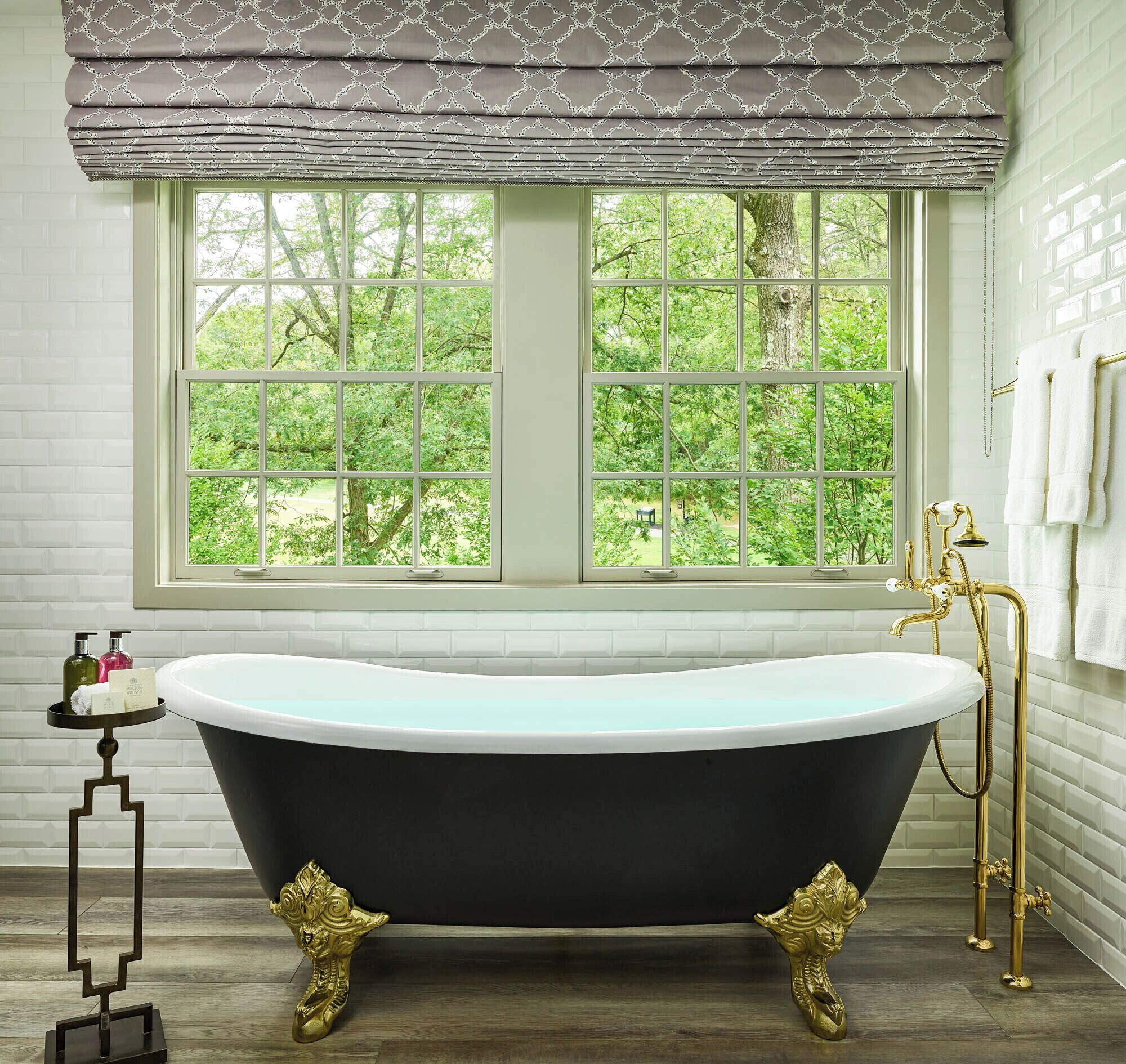 A bathroom with a freestanding bathtub, a window with a view of greenery, and a gold faucet.
