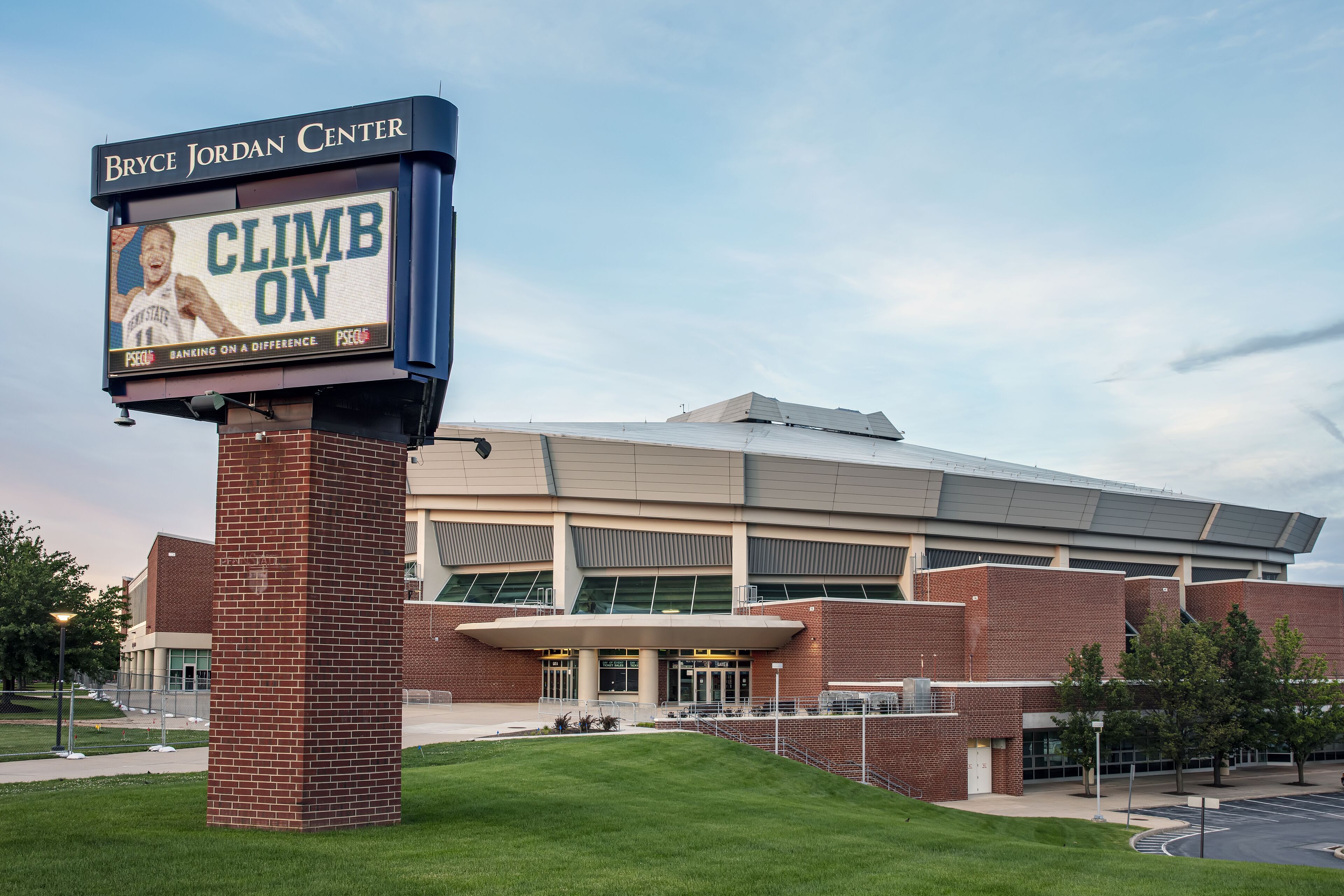 A sports facility with a large digital sign reading "CLIMB ON" and "Bryce Jordan Center" at dusk.