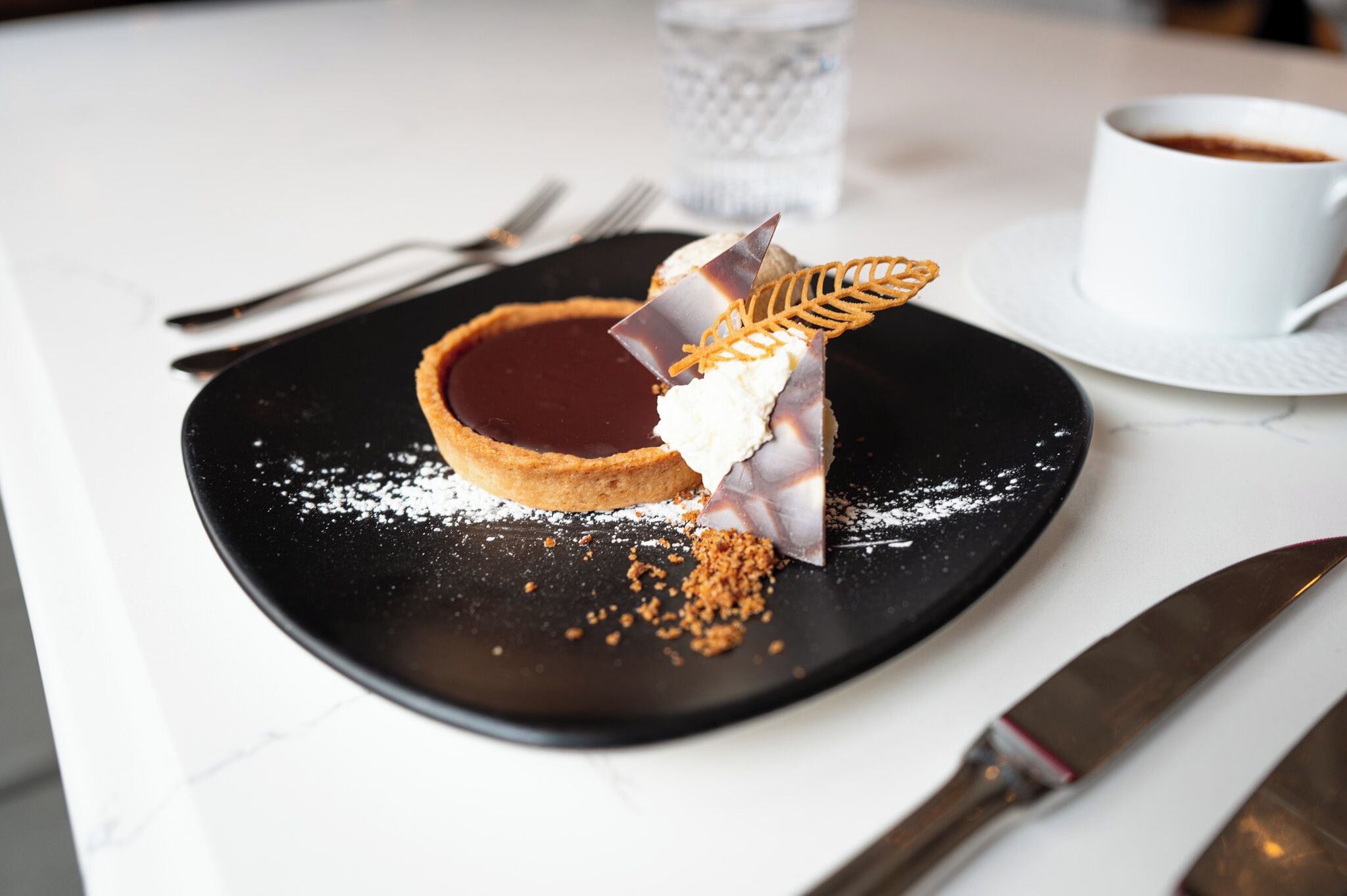 Un postre sobre un plato negro con una taza de café al fondo.