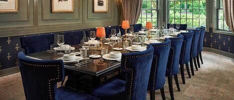 A formal dining room with a long table set for six, blue upholstered chairs, and framed pictures on the wall.