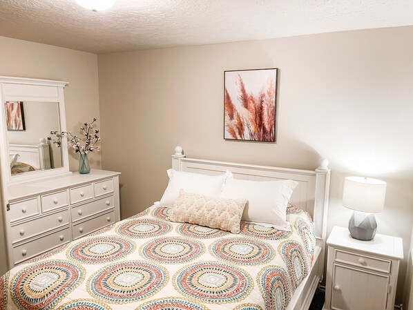 A bedroom with a bed, dresser, nightstand, and a wall-mounted lamp. - Clean, Comfy and Family Friendly Home (away from home) (Meridian)