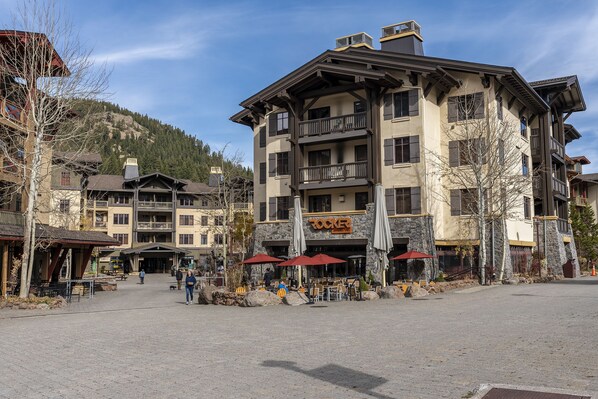 A multi-story building with a restaurant named "Rocker" on the ground floor, outdoor seating with umbrellas, and a mountainous backdrop.