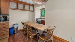 A kitchen with wooden cabinets, a wooden table with chairs, a trash can, and a hanging light fixture.