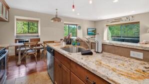 A kitchen with wooden cabinets, a granite countertop, a sink, and a dining area with chairs.