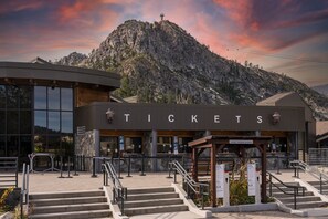 A ticket booth with a mountainous backdrop, featuring a modern building with large windows and a stone facade.