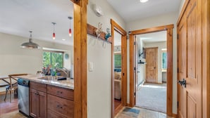 A kitchen with wooden cabinets, a dishwasher, and a countertop with a sink. There is a mirror on the wall and a door leading to another room.
