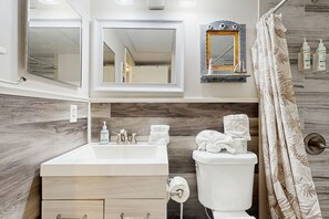 Ein Badezimmer mit einem Holzkonsolenunterschrank, einem Waschbecken, einer Toilette und einer Duschvorhang.