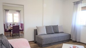 A modern living room with a grey sofa, a white coffee table, and a dining area with purple chairs and a table set for two. - Vacation home Laura by Interhome (Pićan)