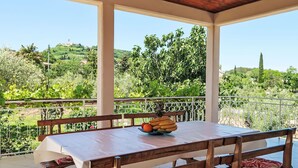 A covered outdoor dining area with a table set for two, benches with patterned cushions, and a view of a lush garden and distant buildings. - Vacation home Laura by Interhome (Pićan)