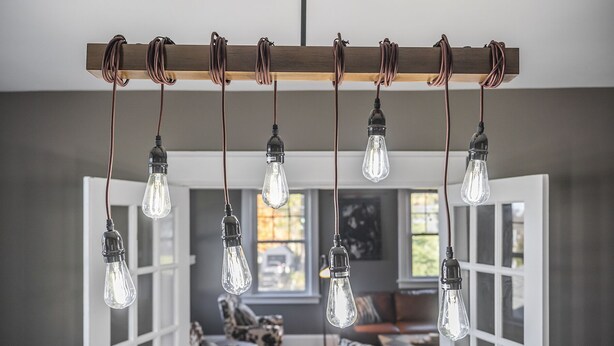 A modern living room with a wooden ceiling rail holding multiple light bulbs, a patterned sofa, and a view through an open door. - Bourbon n Horses themed 3B/2Ba home in beautiful Chevy Chase neighborhood! (Lexington)