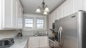 A modern kitchen with white cabinetry, a stainless steel refrigerator, a built-in oven, a microwave, a two-burner stove, a sink, and a window above the sink. - Bourbon n Horses themed 3B/2Ba home in beautiful Chevy Chase neighborhood! (Lexington)