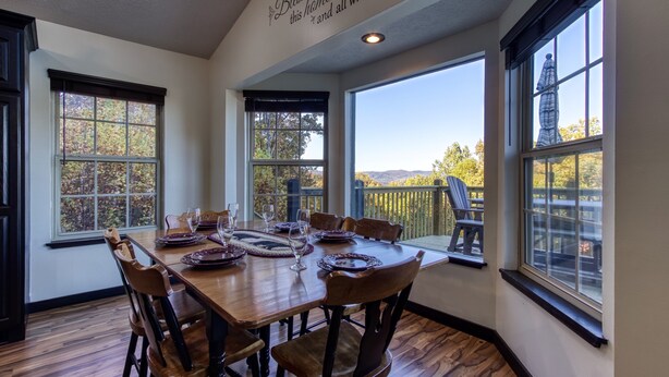 A dining room with a wooden table set for six, large windows, and a view of trees and a statue outside.