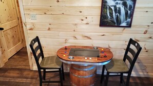 A wooden cabin interior with a rustic wooden table and chairs, a metal barrel stool, and a framed picture of a waterfall on the wall.