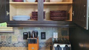 A kitchen with wooden cabinets, a stone backsplash, a knife block, and a toaster.