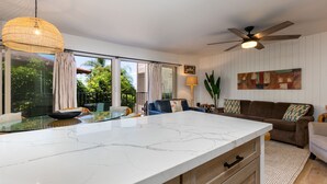 A modern kitchen with a marble countertop, a ceiling fan, and large windows with curtains.