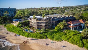 A beachfront hotel with multiple floors, a swimming pool, and lush greenery.