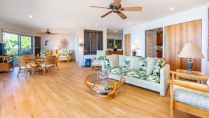 A spacious living room with a large sofa, wicker chairs, a glass coffee table, and a ceiling fan.