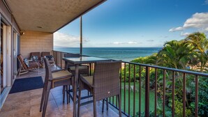 A balcony with wicker furniture, a glass table, and a view of the ocean. - Hale Hui Kai 213 Oceanfront!! (Kihei)