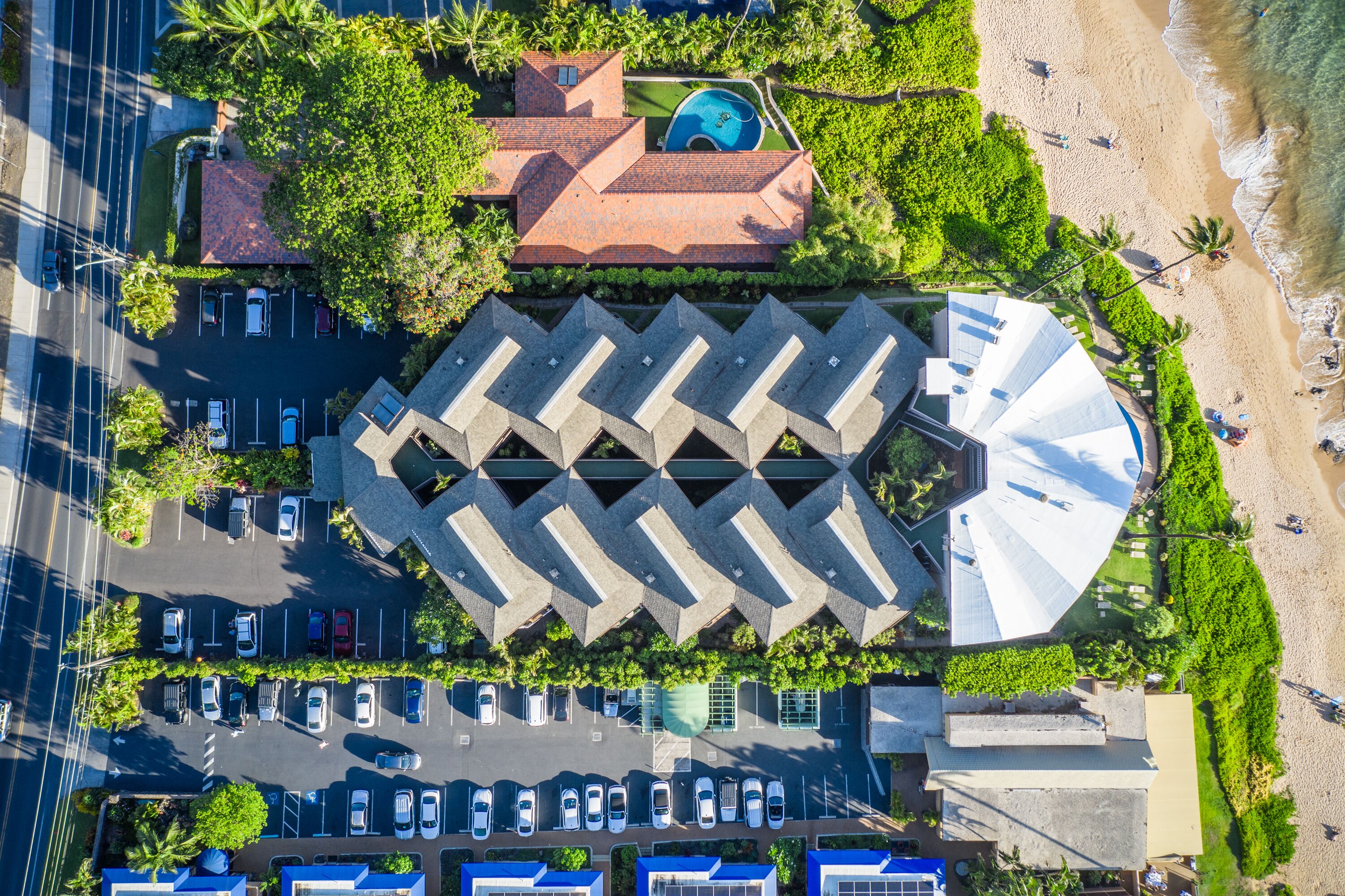 An aerial view of a hotel with a parking lot, a swimming pool, and a beach.