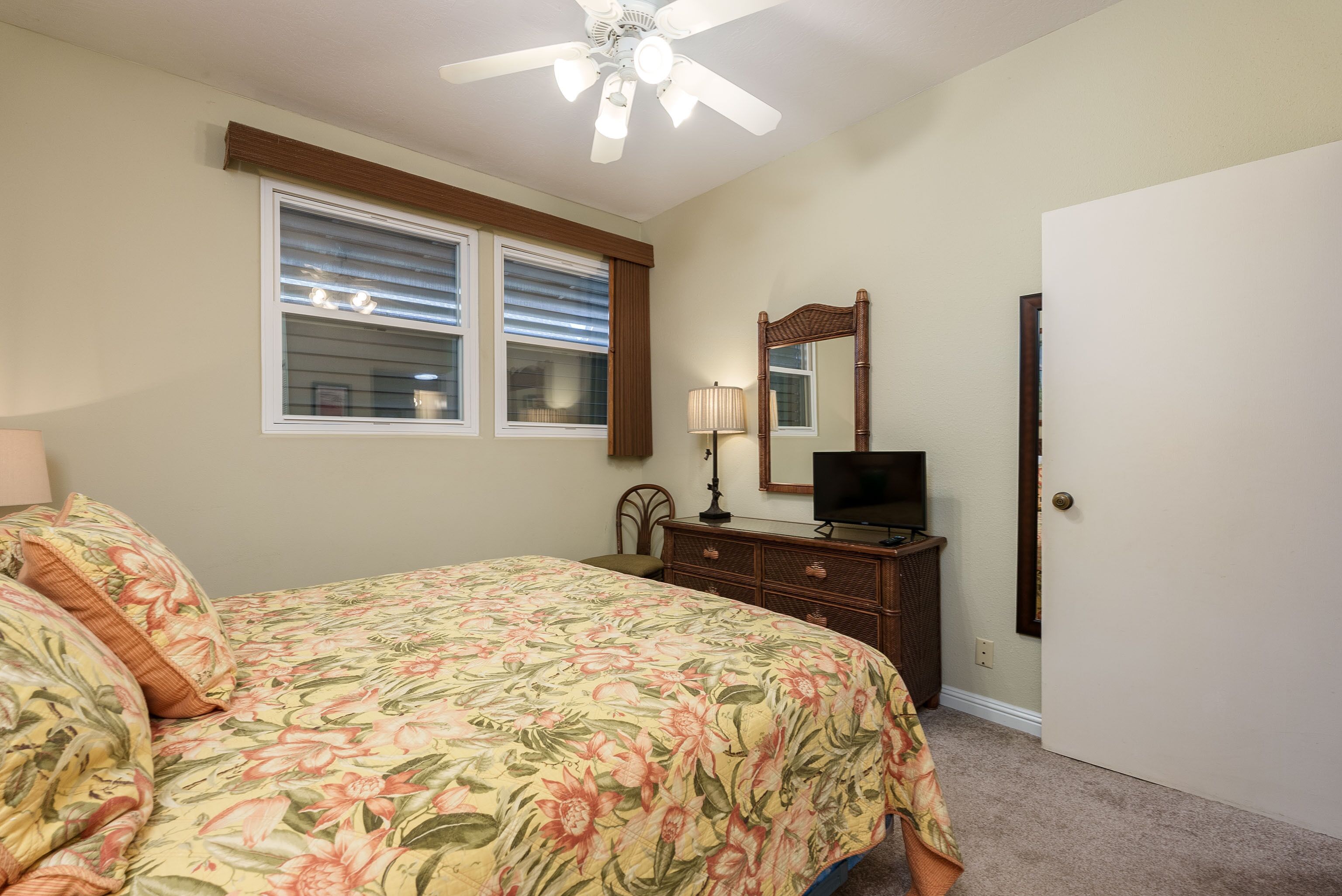 A bedroom with a bed, dresser, mirror, and ceiling fan.