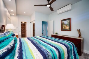 Une chambre à coucher comprenant un lit, un ventilateur de plafond, une commode, un tableau encadré et une porte donnant sur une autre pièce.