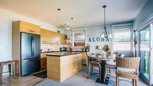 A modern kitchen with a central island, wooden cabinets, a stainless steel refrigerator, and wicker chairs around a table. - Hale Hui Kai 310 Ocean Front Two bedroom / Two bath (Kihei)