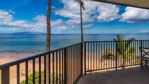 A beach view from a balcony with a railing, palm trees, and a clear sky.