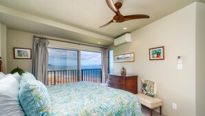 A bedroom with a large bed, a ceiling fan, a view of the beach, and a balcony.