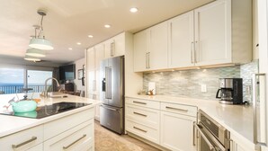A modern kitchen with white cabinetry, stainless steel appliances, a large island, and a view to the outside.