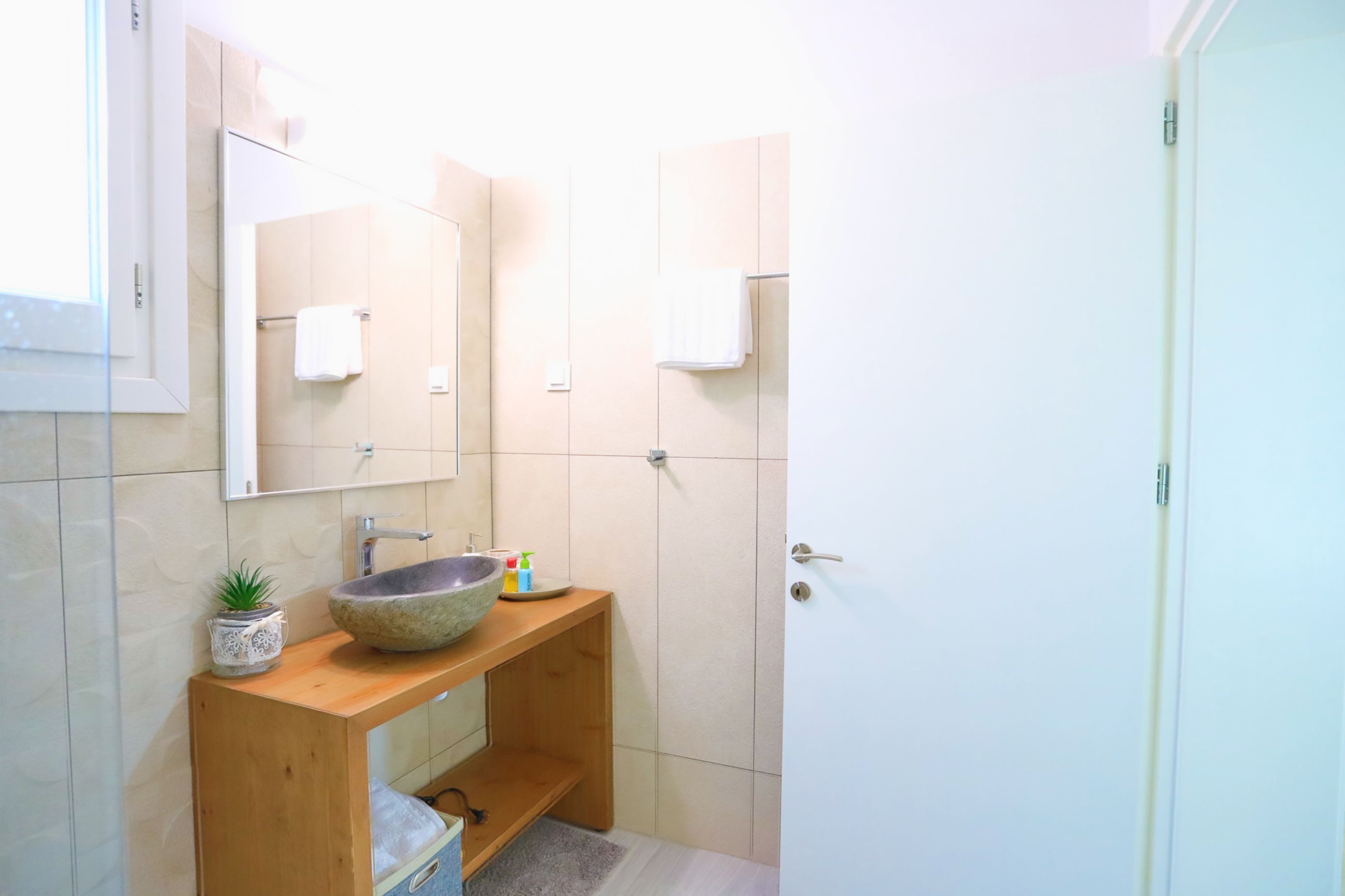 Een badkamer met een houten wastafelmeubel, een stenen wastafel, een kleine plant in een pot en een spiegel boven het meubel.