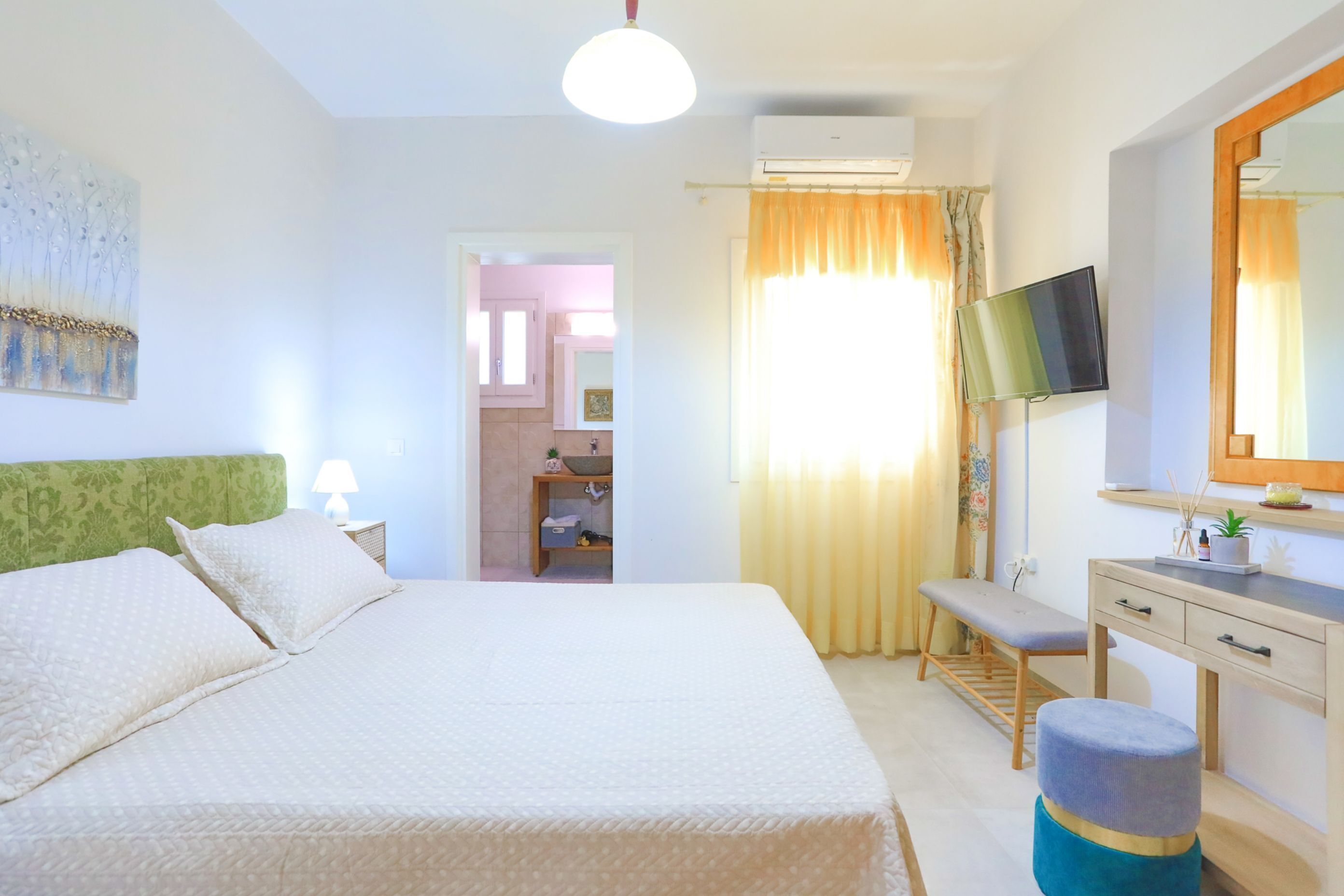 Une chambre d’hôtel avec un lit, un bureau, une télévision, un miroir et une salle de bain visible à travers une porte ouverte.