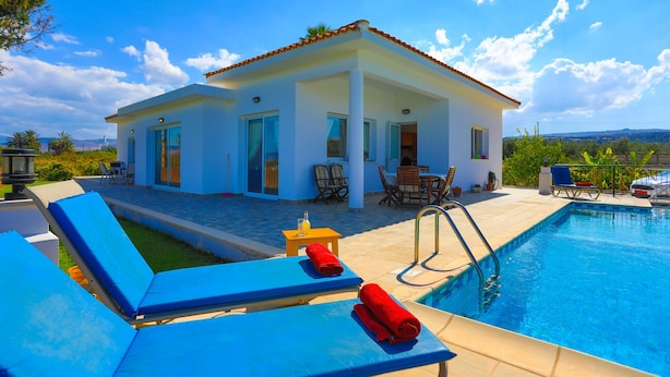 A modern house with a swimming pool, blue lounge chairs, and a patio area with outdoor furniture.