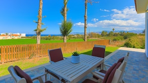 A patio with a table and chairs, a wooden fence, and a view of the sea and mountains.