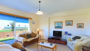 A living room with a sofa, a coffee table, a TV, and a balcony with a view of the sea.