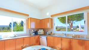 A kitchen with wooden cabinets, a dining table with a patterned tablecloth, and a view of the outdoors through large windows.