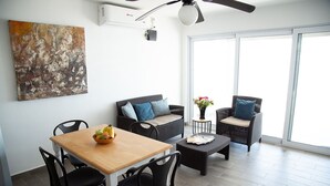 Ein modernes Wohnzimmer mit Esstisch, schwarzen Stühlen, Korbsesseln mit Kissen, einem Couchtisch und einem großen abstrakten Gemälde an der Wand.