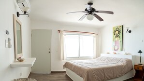 Ein Schlafzimmer mit Bett, Deckenventilator, Fenster mit Vorhängen, Nachttisch und Wandleuchte.