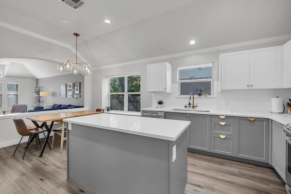A modern kitchen with a central island, grey cabinetry, and a dining area with a wooden table and chairs.