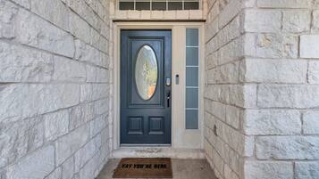 A stone-walled entrance with a dark door featuring a glass panel and a doormat with text.