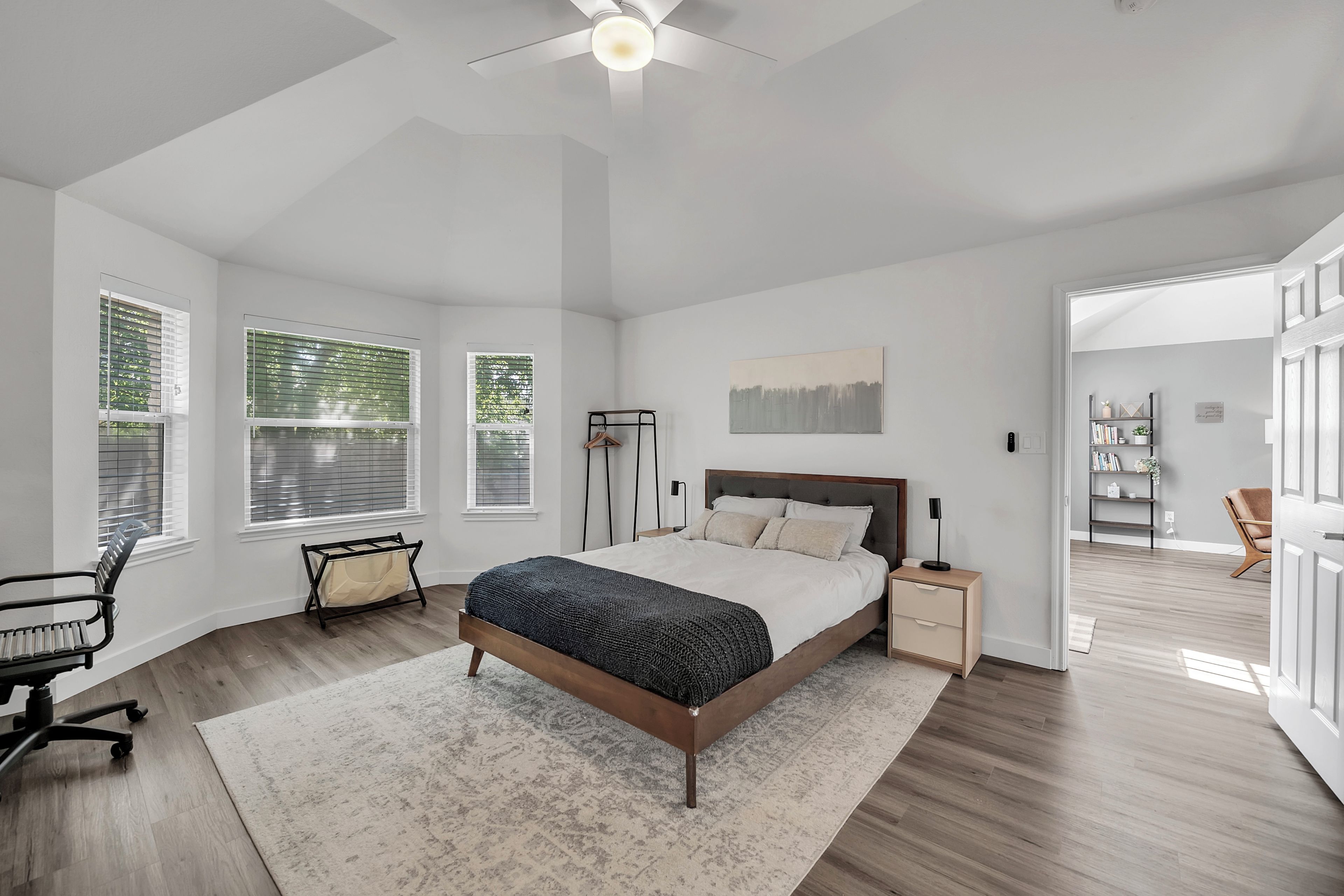 A bedroom with a large bed, a desk, a chair, and a ceiling fan.