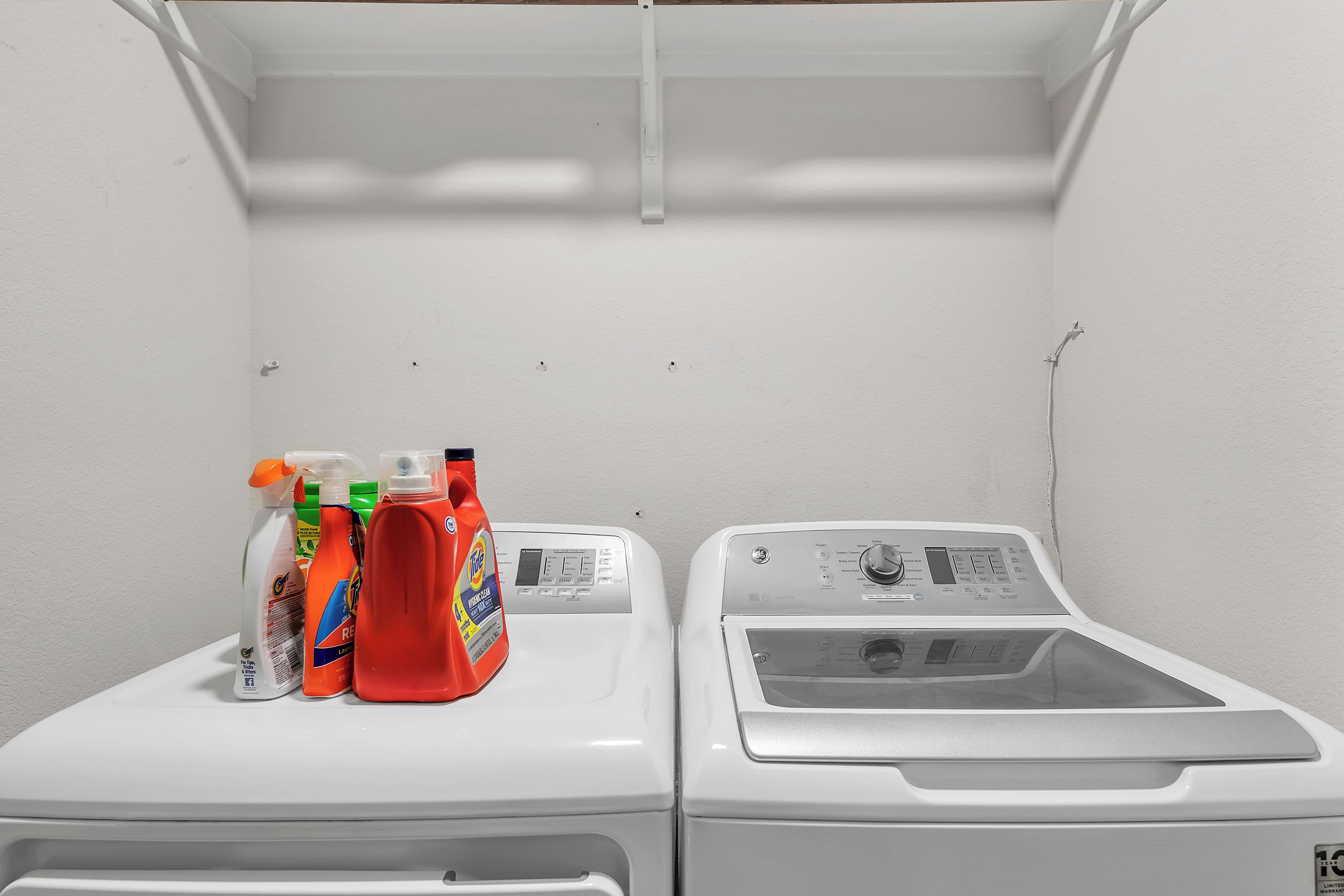 A laundry room with two washing machines and a shelf with cleaning supplies.