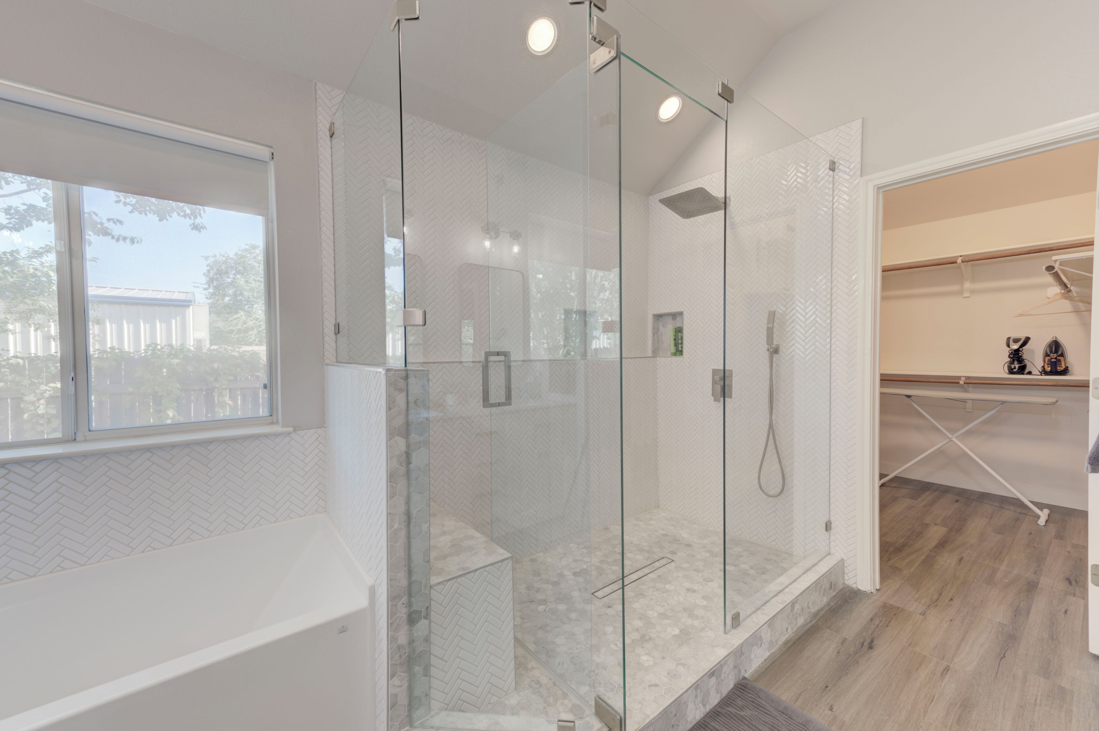 A modern bathroom with a glass-enclosed shower, a window, and a wooden floor.