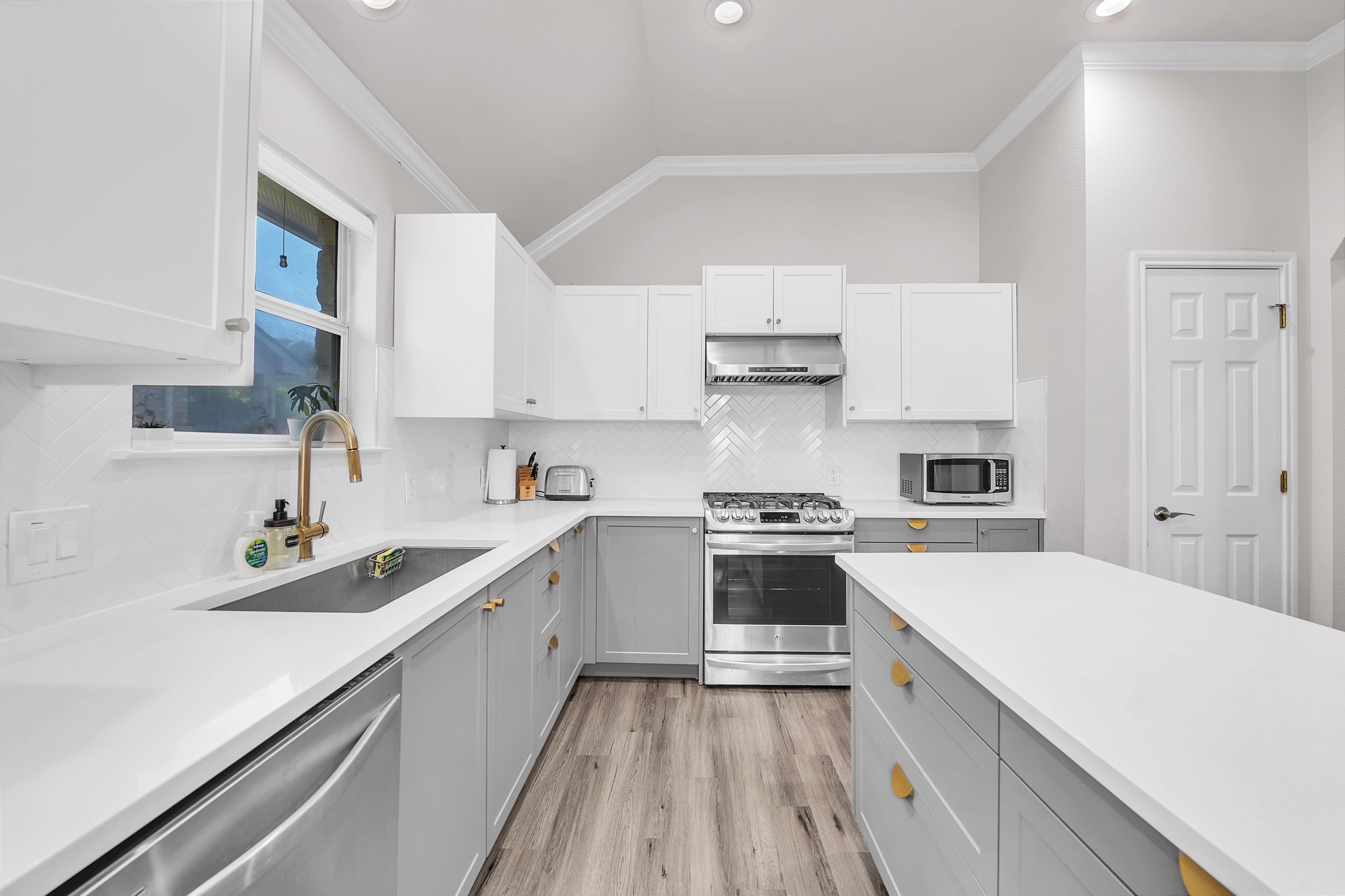 A modern kitchen with white cabinetry, a stainless steel stove, a microwave, and a window with a view.