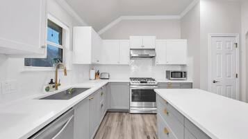 A modern kitchen with white cabinetry, a stainless steel stove, a microwave, and a window with a view.