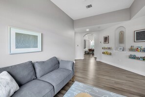 A modern living room with a grey sofa, a patterned rug, and a hallway leading to a dining area.